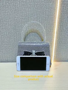 Mini silver rhinestone evening bag with black bow tie detail next to a smartphone