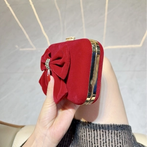 Detail view of red velvet clutch bag with a large rhinestone bow and gold metal frame