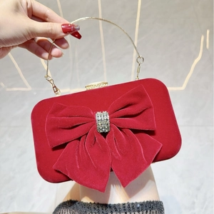 Close-up of red velvet evening bag with diamond bow and gold metal handle
