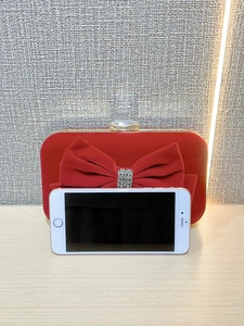 Detail of red velvet evening clutch with oversized rhinestone bow and phone size comparison