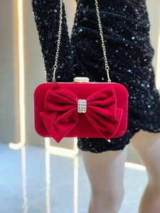 Close-up of red velvet clutch bag featuring a crystal bow and elegant gold chain strap