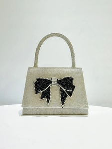 Detail of silver rhinestone evening bag featuring a large black crystal bow and top handle
