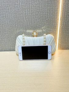 Size comparison of white satin evening bag with pearl handle next to an iPhone