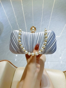Detail of silver pleated evening clutch with large pearl handle and luxury gold clasp
