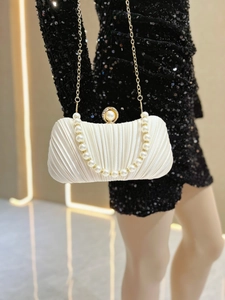 Close-up of pleated ivory satin clutch with pearl trim and gold chain strap detailing