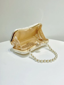 Detail of open satin pleated evening bag with pearl handle and rhinestone clasp