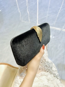 Elegant black evening clutch bag with a golden leaf clasp held by a woman in a formal setting