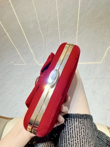 Red velvet evening clutch bag with bow and crystal clasp held by model against marble