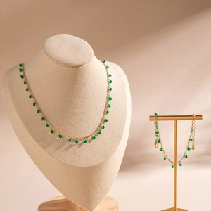 Golden necklace and bracelet set with green beads on neck model display stand