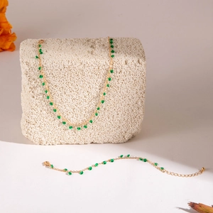 Detail of gold necklace and bracelet set with green beads on a white stone background