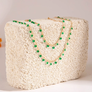 Detail of emerald green faceted beads and gold chain draped over a white coral stone