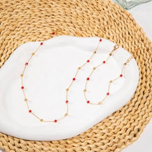Detailed view of gold chain jewelry set with red cubic beads on a ceramic tray