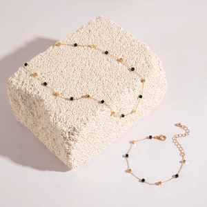 Detail of gold necklace and bracelet set with black cubic beads on white stone decor