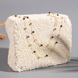 Detailed view of a gold-tone necklace with black and gold beads on a white stone slab