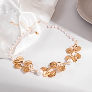 Détail macro de la texture des feuilles dorées et des perles sur ce collier élégant