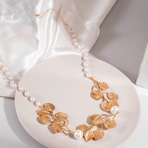 Détail d'un collier de perles avec feuilles dorées sur un plateau en céramique