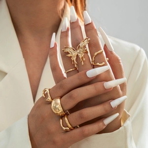 Detailed view of layered gold flower and butterfly rings on model with long nails