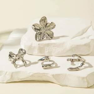 Detailed view of silver flower and bow rings set on white stone with soft shadows