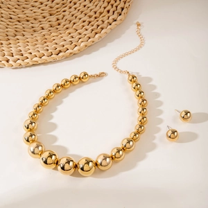 Dettaglio della collana con grandi sfere dorate lucide e orecchini coordinati alla moda