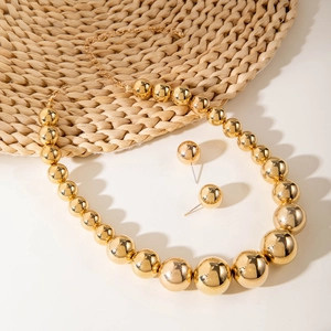 Set collana e orecchini con grosse perle dorate e finitura lucida su stuoia in paglia