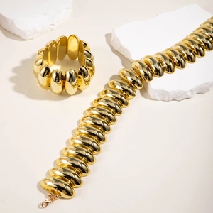Dettaglio di collana e bracciale a maglie larghe dorate lucide su pietra