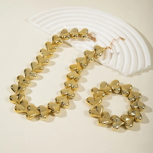 Polished gold heart charm necklace and bracelet set on an elegant artistic background