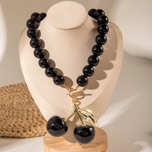 Macro detail of black acrylic beads with golden leaf cherry pendant and toggle clasp