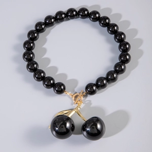 Detail of glossy black acrylic beaded necklace with golden cherry pendant and toggle clasp