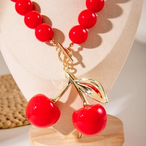 Close-up of vibrant red acrylic beads and golden leaf cherry pendant on heart stand