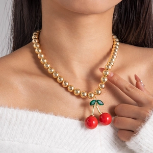 Detail of a cherry pendant necklace with red acrylic beads on a gold bead chain
