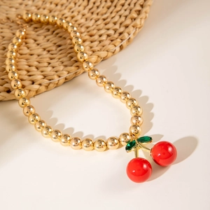 Detail view of golden metal beaded necklace with vibrant red cherry pendant