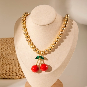 Close-up of golden beaded necklace featuring a red cherry pendant on a beige jewelry bust