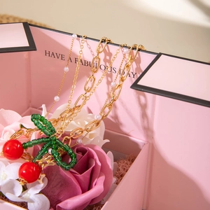 Detailed view of cherry pendant necklace with pearls and gold chains in a pink gift box