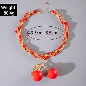 Detail of red cherry pendant necklace with gold chain and ribbon woven texture