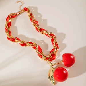 Macro detail of gold-tone chain necklace with red ribbon and shiny cherry pendant