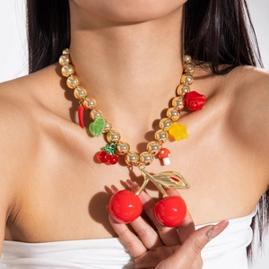 Detail of chunky gold beads necklace with oversized red cherry and mixed fruit pendants