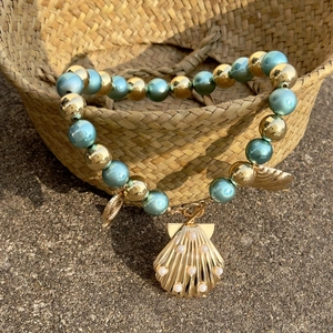 Macro detail of a summer ocean-style necklace with light blue beads and a gold shell pendant