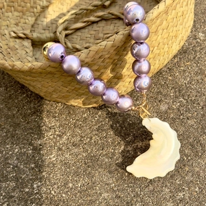 Detail of beaded lavender pearl necklace featuring a cream conch shell pendant on straw basket