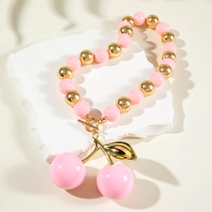 Detail of pink acrylic beads and cherry pendant necklace with gold OT buckle on a stone plate