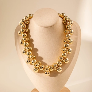 Macro shot of chunky gold metallic bead cluster necklace on a beige jewelry display stand