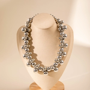 Close-up of metallic chunky bead choker necklace on beige velvet display bust