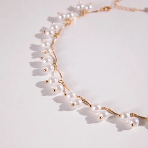 Detail of wavy gold metal chain interlaced with elegant white pearls on a grey background