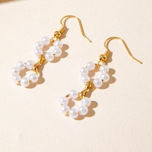Detailed shot of long gold earrings featuring elegant double imitation pearl circles