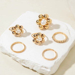Detail of baroque pearl flower rings and gold stacked ring set on white stone pedestal
