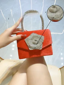 Detail view of a luxury red evening bag featuring a 3D rhinestone rose and crystal handle