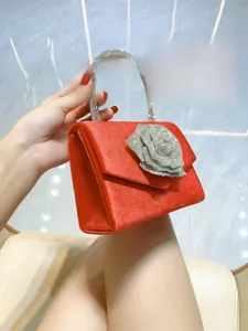 Detail of red velvet evening clutch featuring a silver rhinestone rose and circular handle