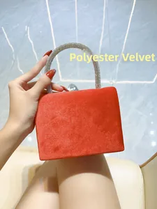 Detail of red velvet evening bag featuring a crystal-encrusted curved handle for women