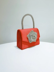 Detail of red satin evening bag featuring a silver rhinestone rose and crystal handle