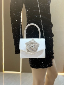 Detail of white satin evening bag featuring a large 3D rose and rhinestone handle