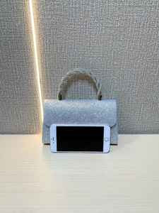 Silver sequin clutch bag detail showing size comparison with a white smartphone